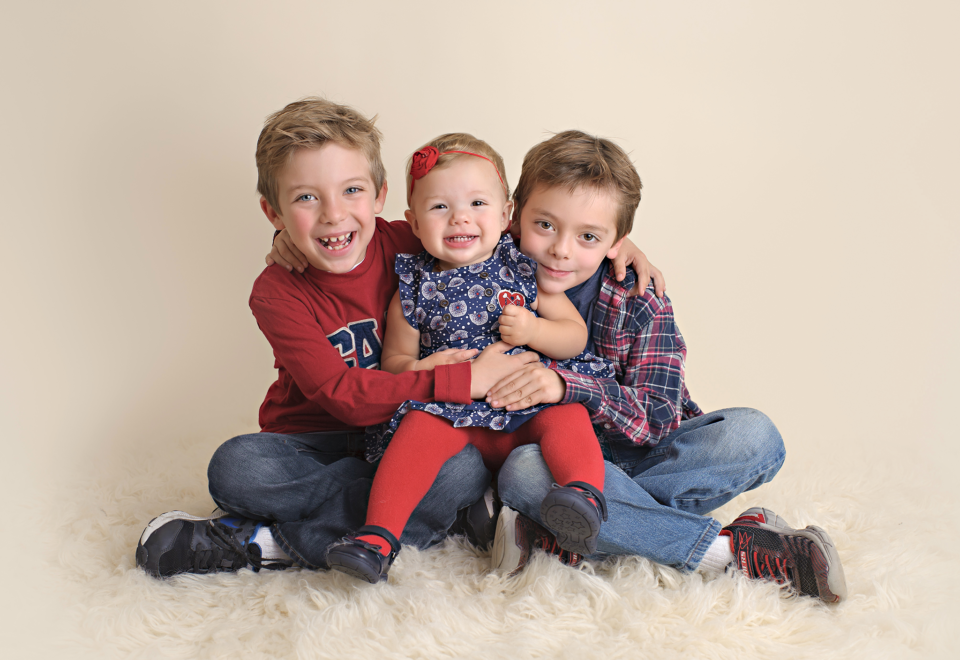 two brothers holding their baby sister in a studio setting for their Christmas card