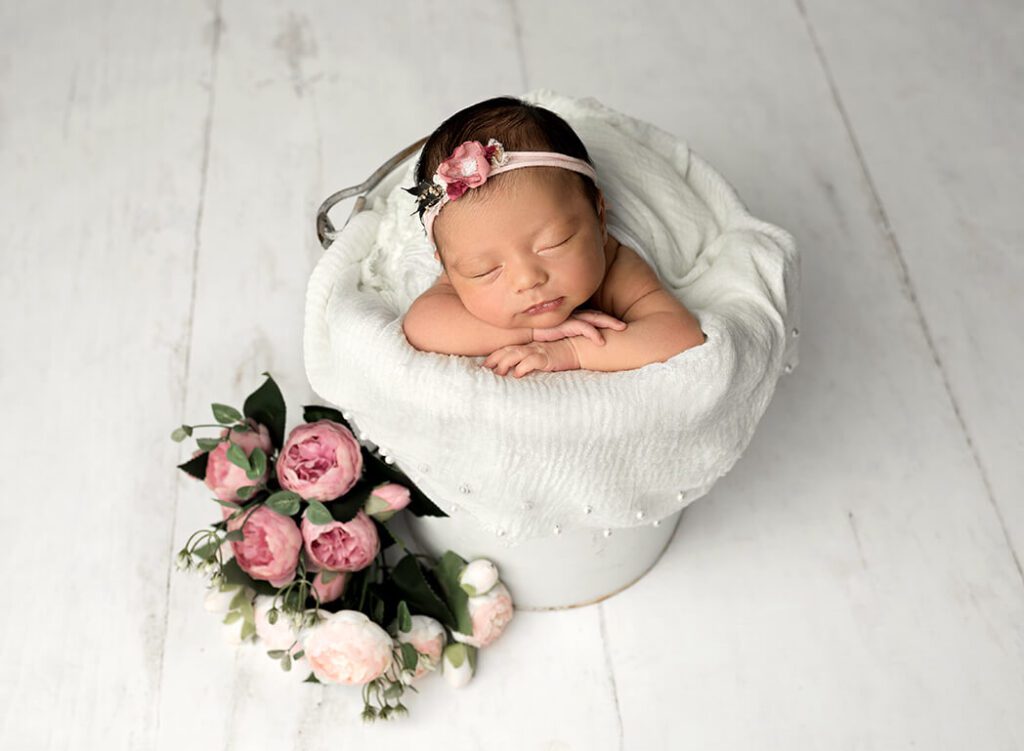Sweet moment of baby girl posed in a bucket surrounded by florals