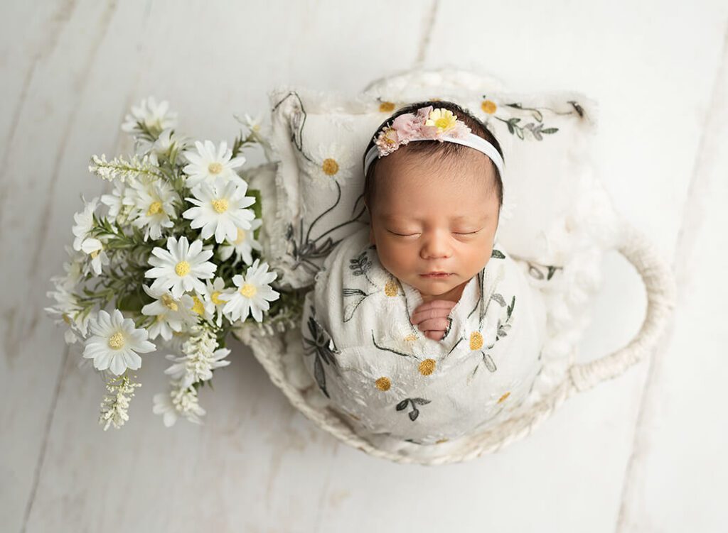 baby girl posed in a basket surrounded by flowers, and wrapped in a floral wrap